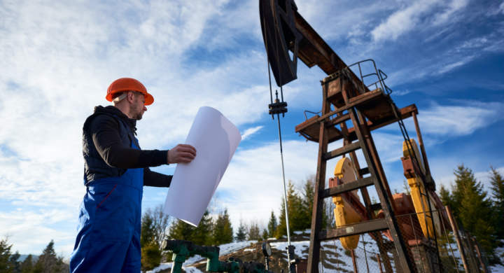 oil-worker-standing-in-the-oilfield-next-to-a-pump-jack-with-a-big-paper