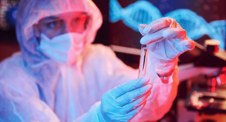 nurse-in-mask-and-white-uniform-holding-tube-with-liquid-and-sitting-in-neon-lighted-laboratory-with-computer-and-medical-equipment-searching-for-coronavirus-vaccine