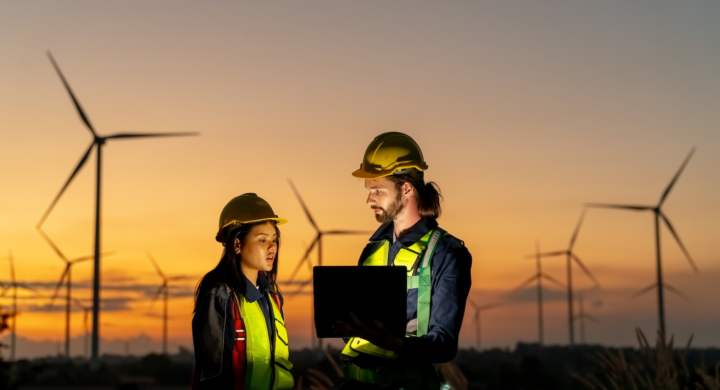 multiracial-colleagues-examining-wind-turbines-blueprints-windmills-on-sunset