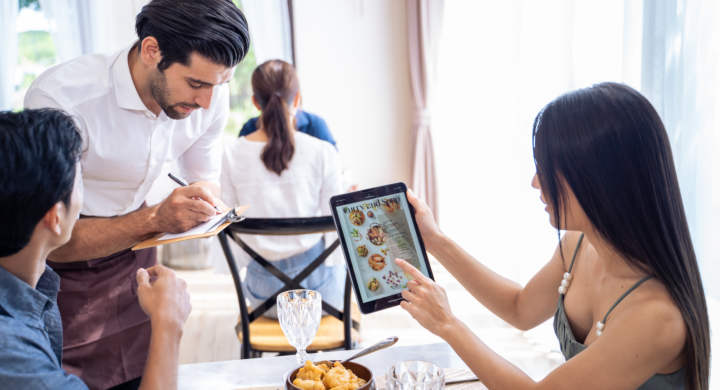 Caucasian waiter receiving order serving from customer in restaurant. Attractive server service man working, taking note, writing order from consumer with pen at table in dining room with happiness.