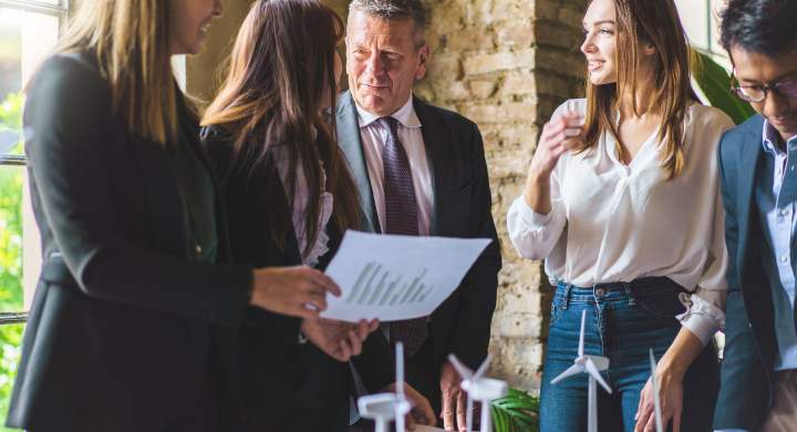 young-entrepreneurs-talking-about-renewable-energy-project-standing-around-a-table-holding-data-paperwork