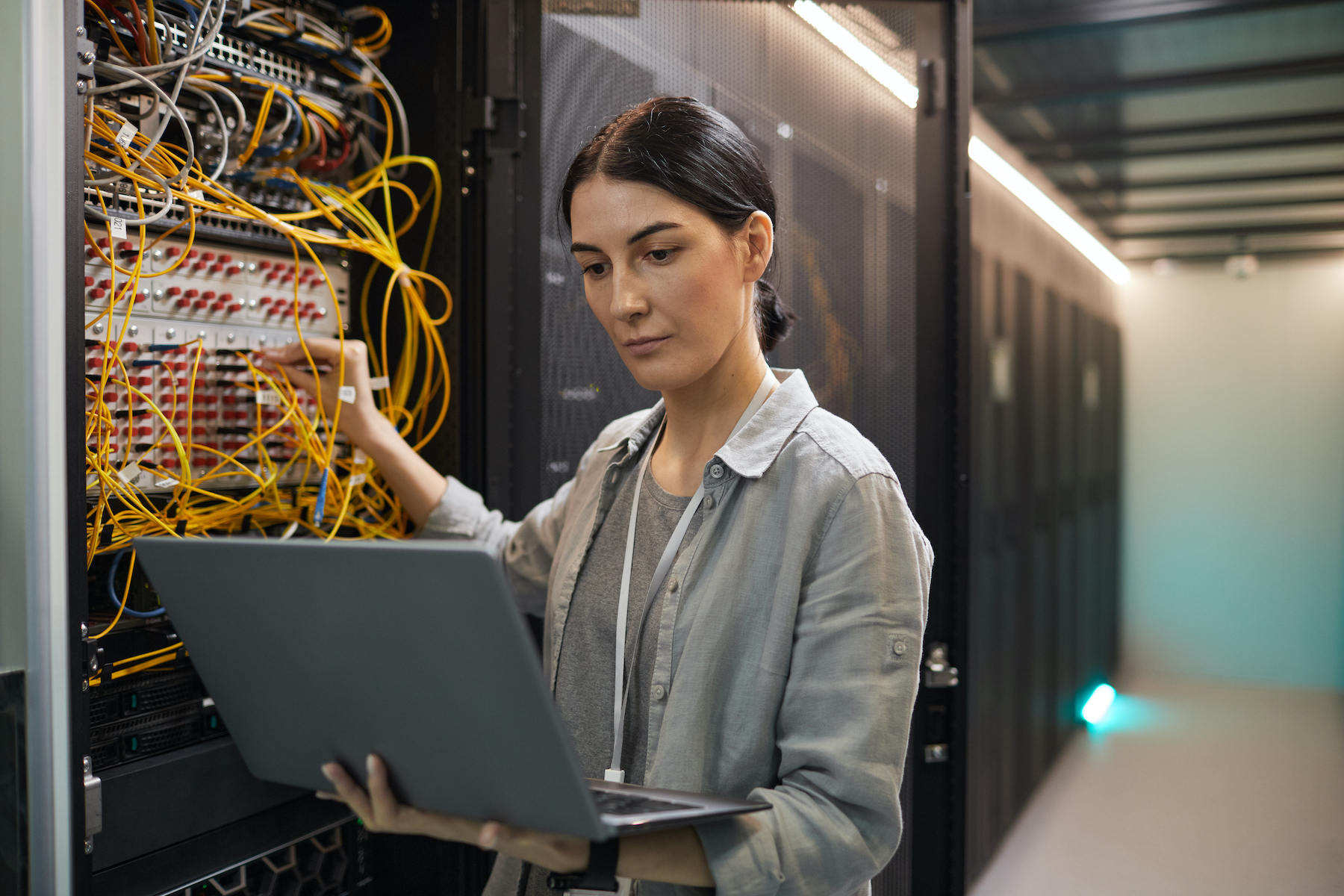 Waist up portrait of female network engineer connecting cables in server while working with supercomputer in data center for AI.