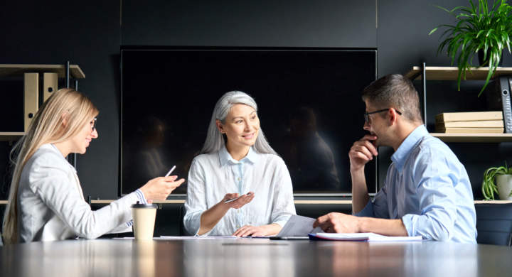 senior-asian-female-mentor-talking-to-younger-colleagues-interns-in-office