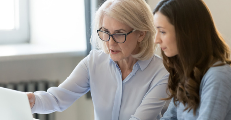 two women, one older and one younger, in a professional setting, looking at something on a laptop