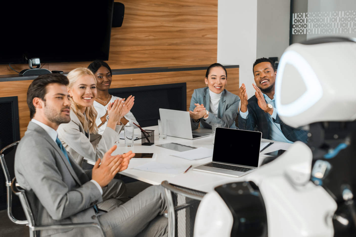 selective focus of multicultural businesspeople applauding while looking at robot in office