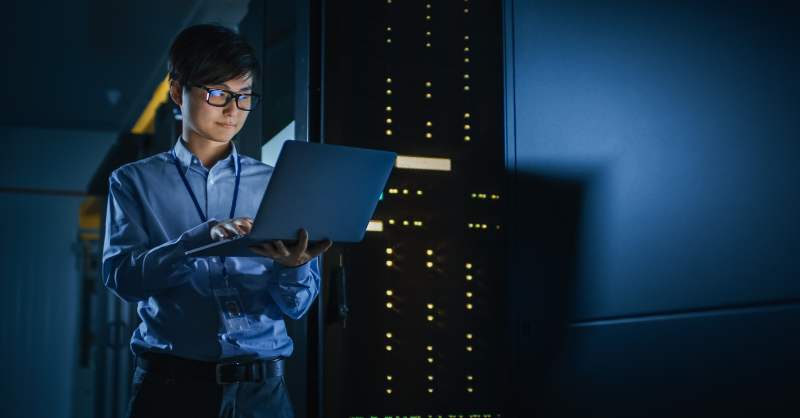 woman with computer standing in front of servers