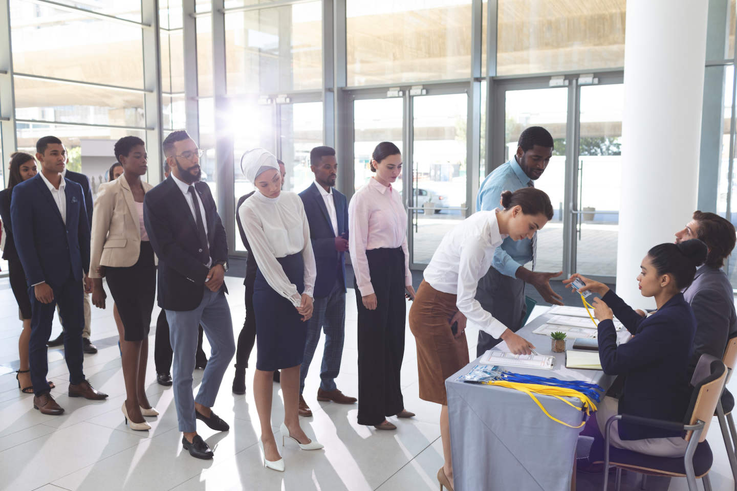 Side view of diverse business people checking in at conference registration table while mixed-race businesswoman wearing hijab looks at table in office lobby