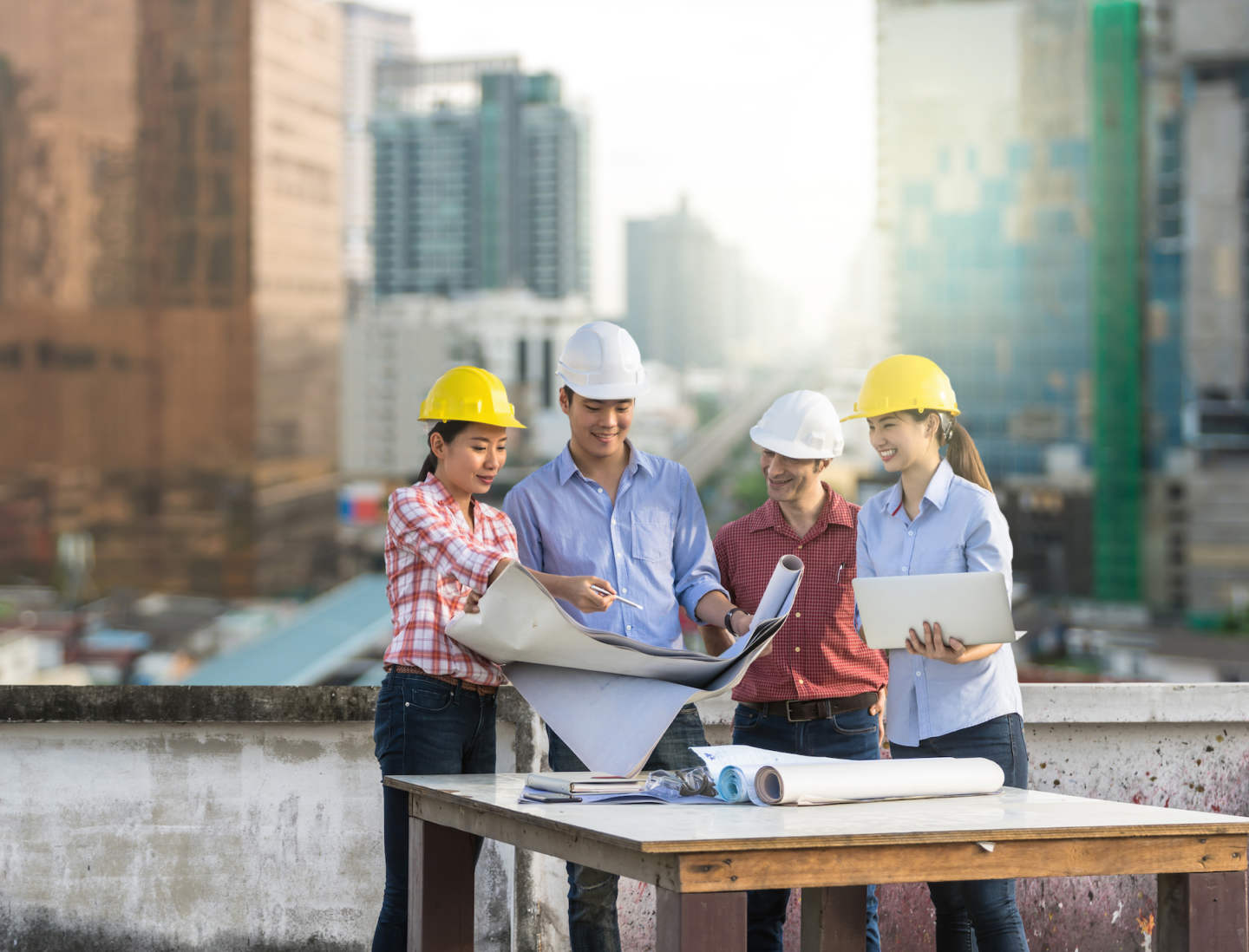 Happy professional construction engineers working with Corporate Colleagues Teamwork and equipment blueprint and laptop at the building site place over the sky train with cityscape background