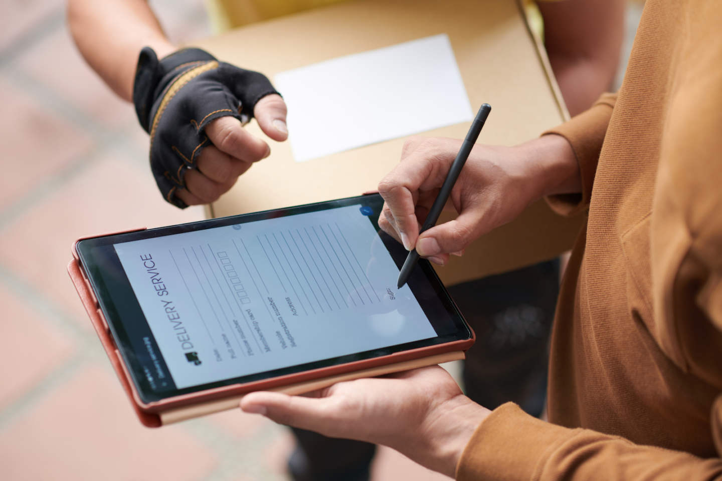 Close-up of man signing the form on digital tablet while getting the parcel from delivery person