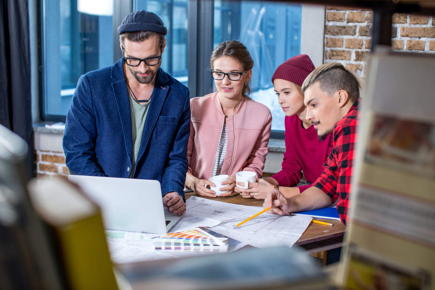 Four young stylish designers working at project in office looking on laptop