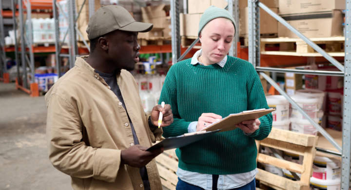 Mature woman checking list and discussing shipping together with her colleague during work at warehouse