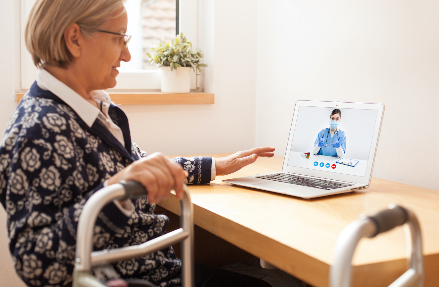 Retired senior elderly woman with mobility problem talking to UK NHS GP female doctor via virtual telemedicine video call,holding walking frame,online appointment therapy treatment,telehealth concept