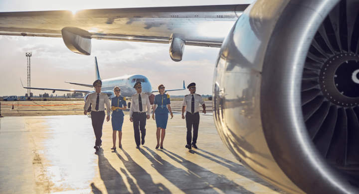 Full length portrait of flight team wearing business uniform walking near the passenger airplane in the outdoors