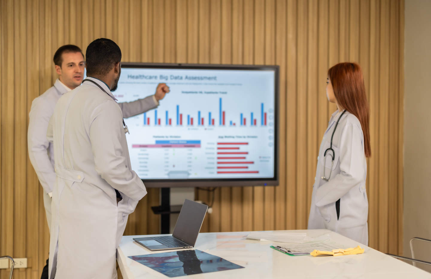 Team of doctors discuss healthcare big data to analyze patient satisfaction trends, waiting status, turnover rates aiming to identify areas for improvement, create cost effective management plans.