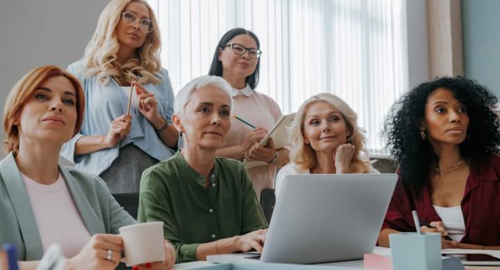 Group of mature women listening to speaker while having business training in office