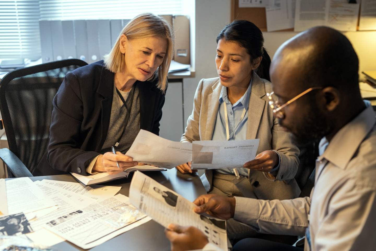 Two intercultural female agents comparing information in criminal profiles while discussing personal data of suspects