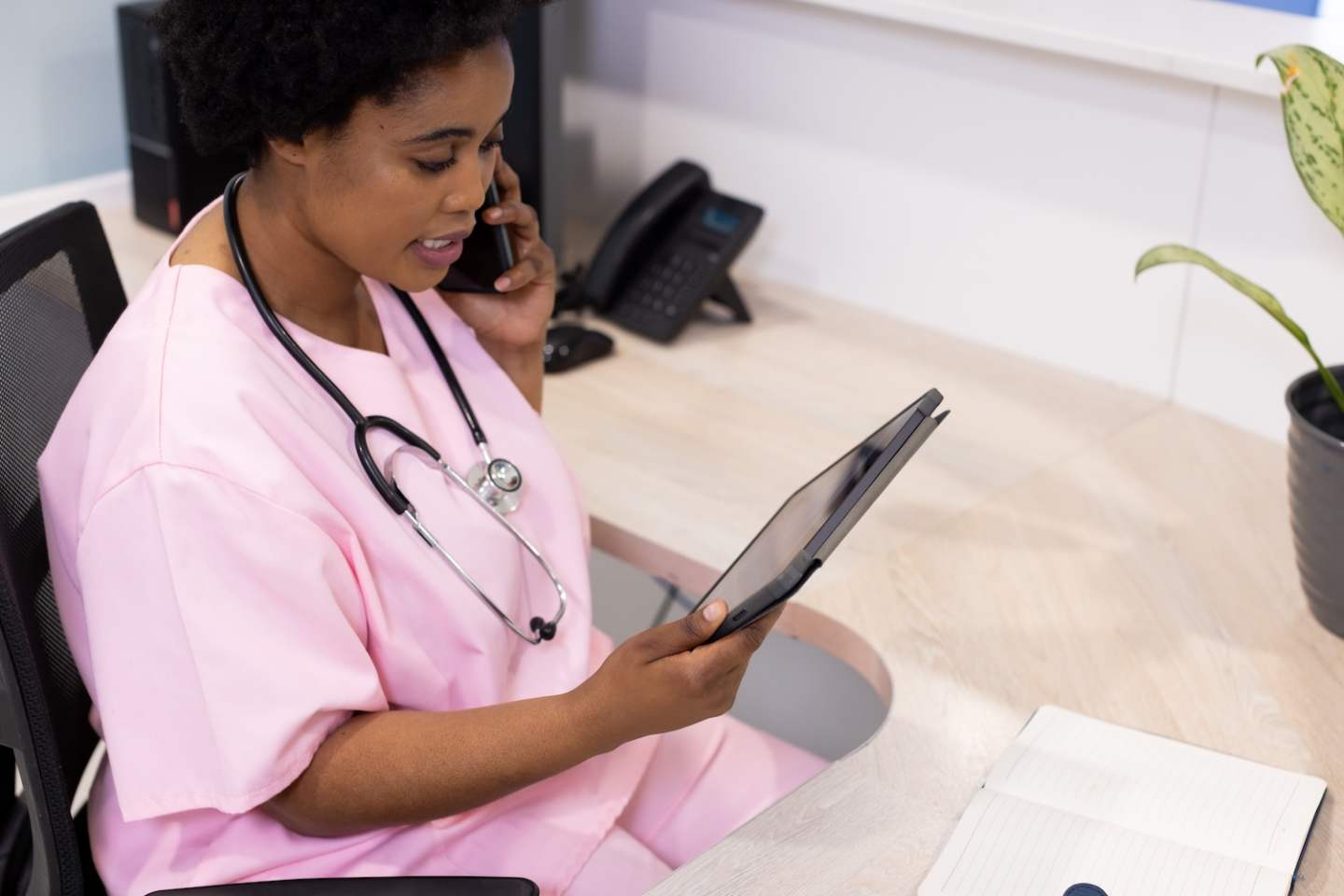 African american female doctor talking on smartphone and using tablet in hospital reception. Medicine, healthcare, communication and medical services, unaltered.