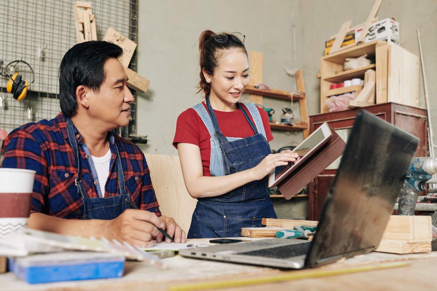 Smiling young female carpenter showing coworker tablet computer with furniture item draft on ther screen that she was working on