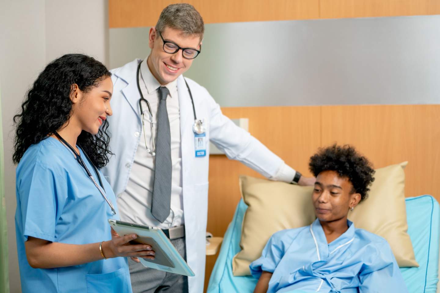 Nurse hold tablet and also explain the treatment result to patient who lie on bed and he look happy after know good result.