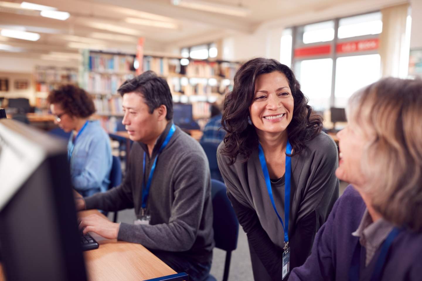 Teacher With Group Of Mature Adult Students In Class Working At Computers In College Library