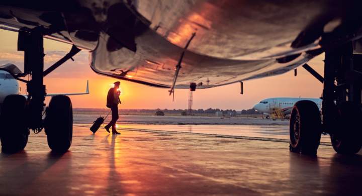 Full length portrait of part of passenger airplane with pilot isolated on sunset background