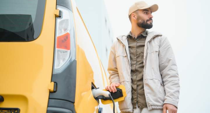 Casual man near electric car waiting for the finish of the battery charging process.