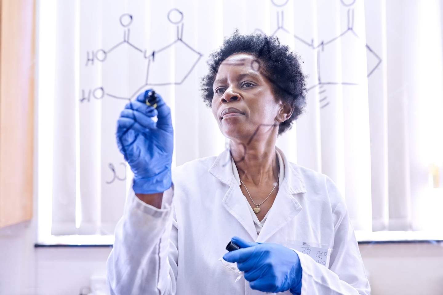 Shot of a female scientist drawing molecular structures on a glass wall in a lab.