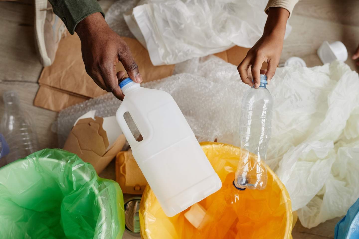 Top view close up of African-American father and son putting plastic in recycling bins at home, copy space
