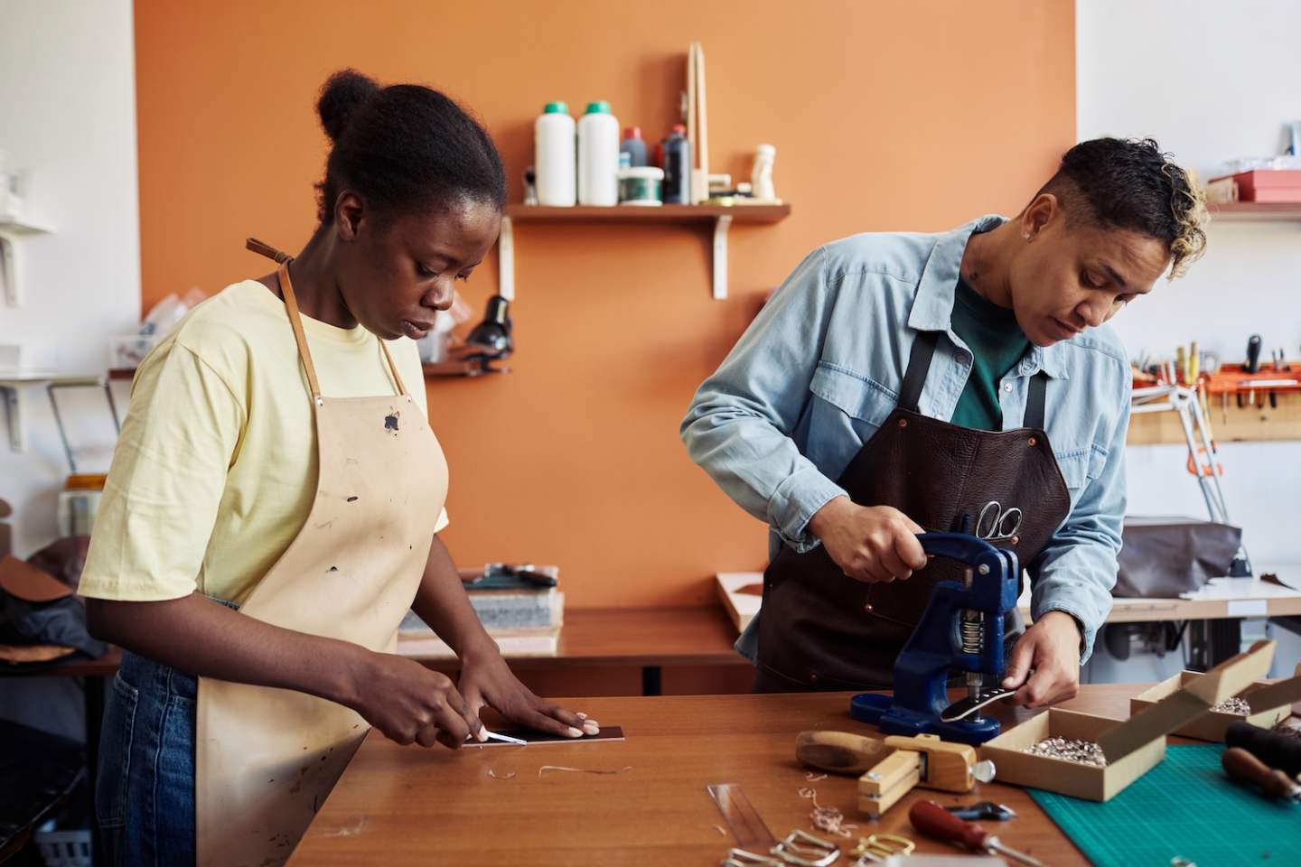 Side view portrait of two multiethnic young women working with leather in workshop and creating handmade pieces