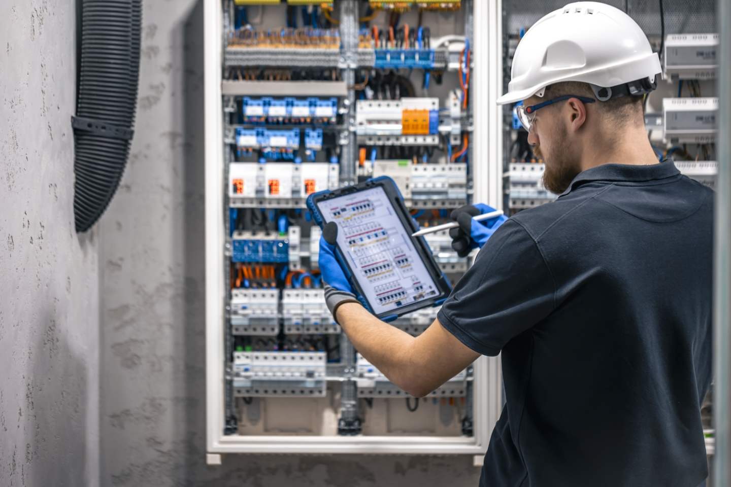 Electrical technician working in a switchboard with fuses, uses a tablet. Electrical technician looking focused while working in a switchboard with fuses.