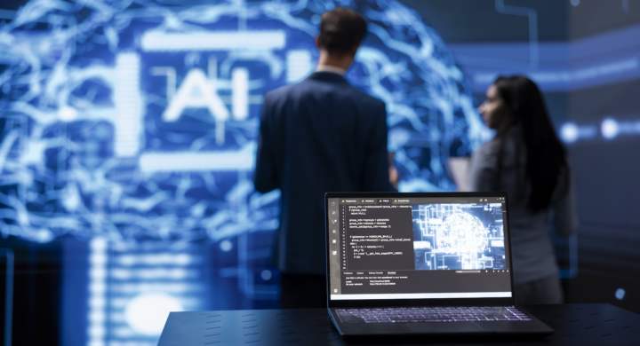 Focus on laptop running AI cognitive computing tech used by IT staff members in blurry background. Close up of notebook used by teamworking engineers to do data mining with self learning algorithms