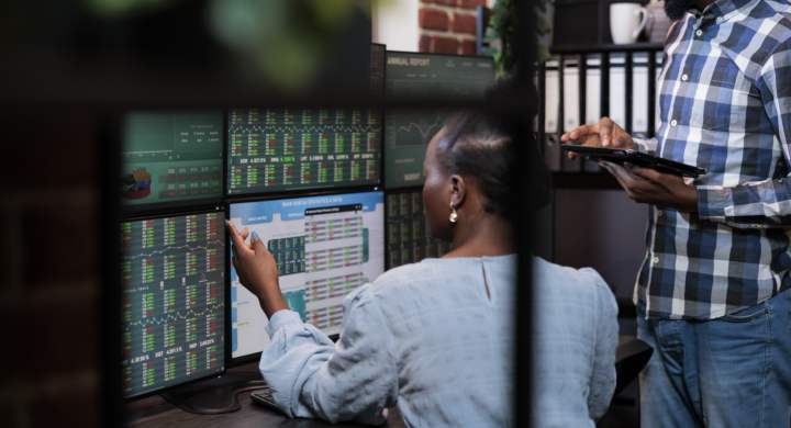 Investment company employees sitting at multi monitor workstation while analyzing real time trend charts. Forex stock market traders talking about capital budget and statistics charts.