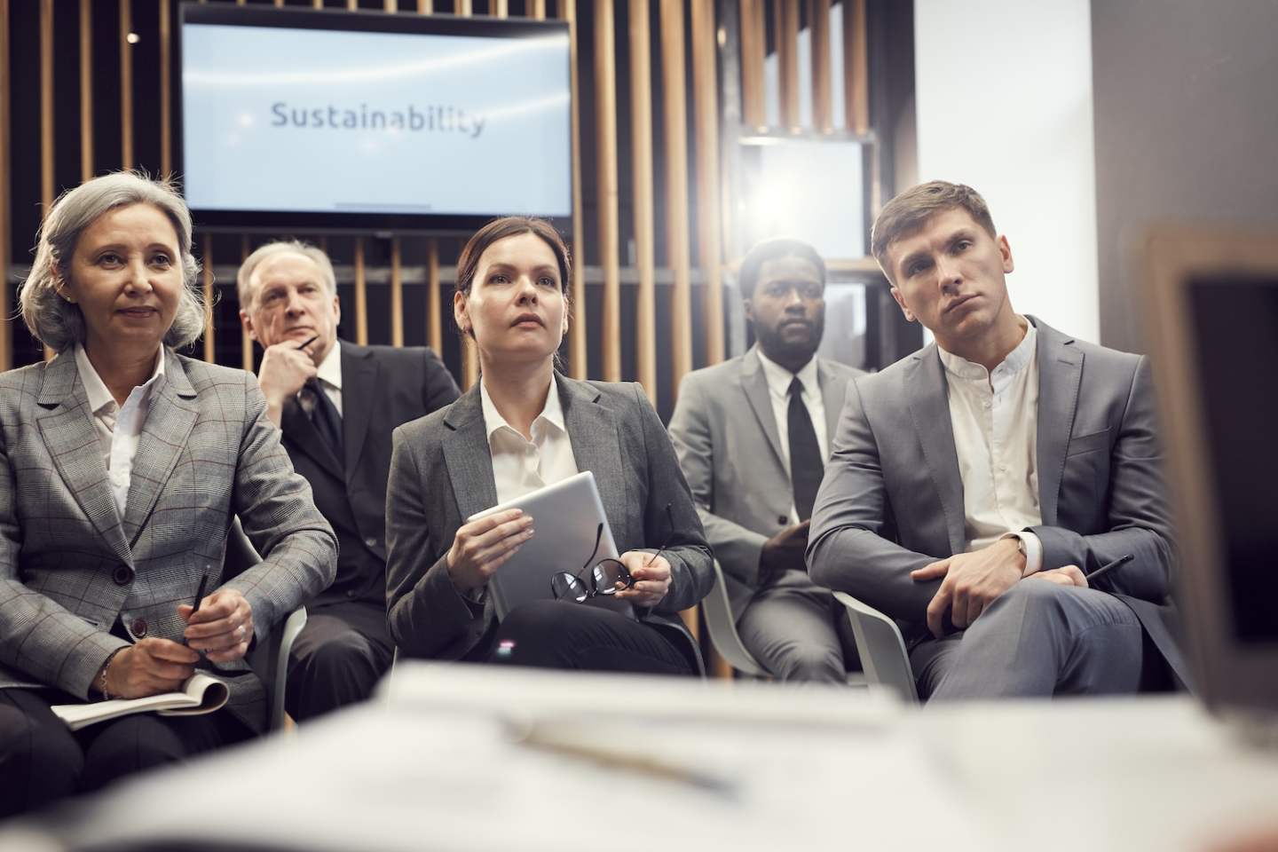 Group of serious multi-ethnic business people in formalwear sitting in conference room and attentively listening to speaker