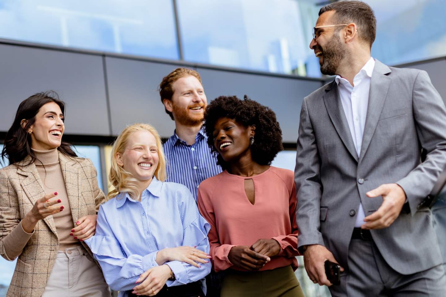 A group of businness people colleagues gathers for a casual conversation outside a contemporary office, reflecting teamwork and connection.