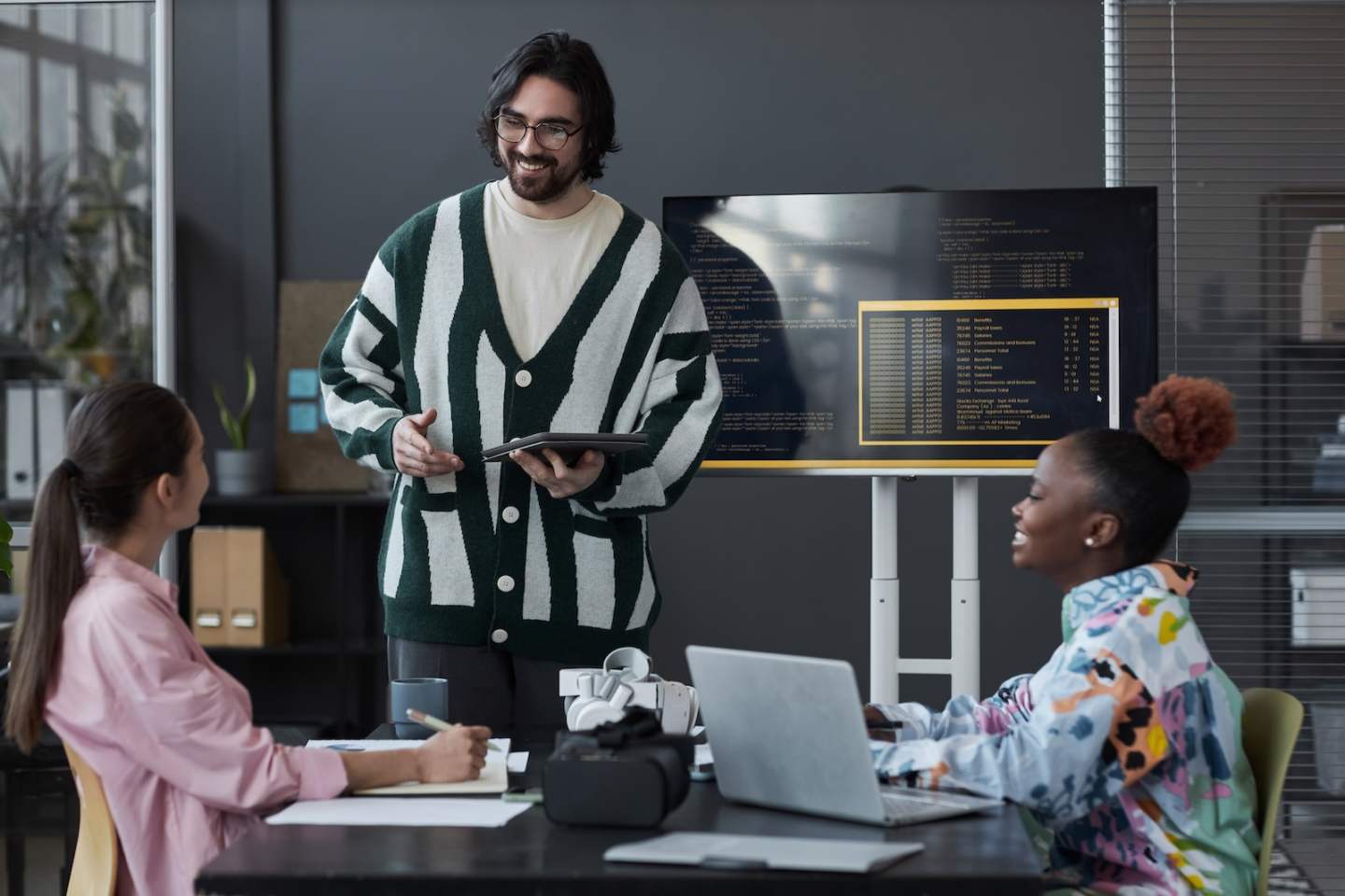 Young developer standing near the screen with codes and presenting his report to colleagues during teamwork in office