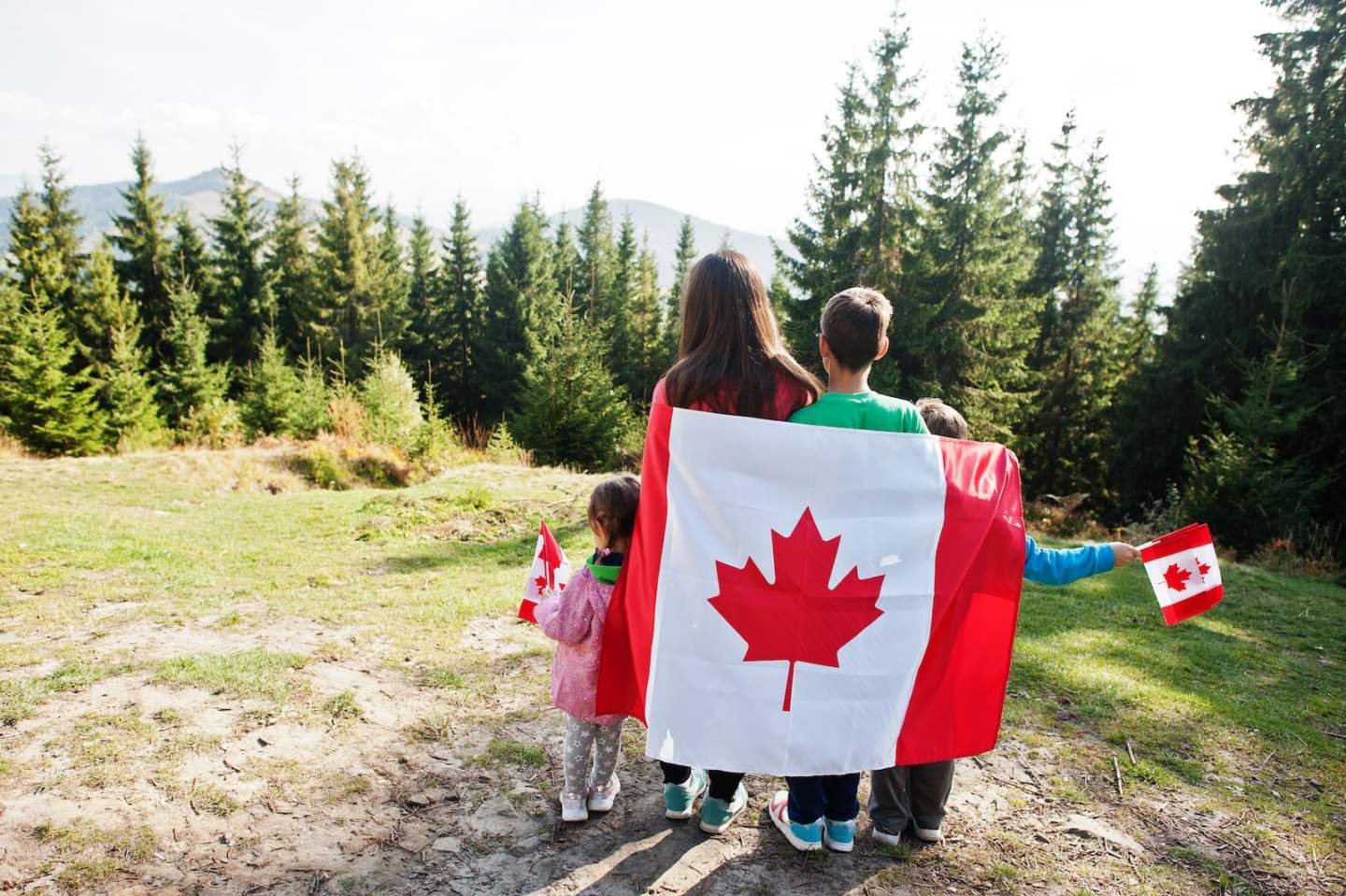 Happy Canada Day. Family of mother with three kids hold large Canadian flag celebration in mountains.
