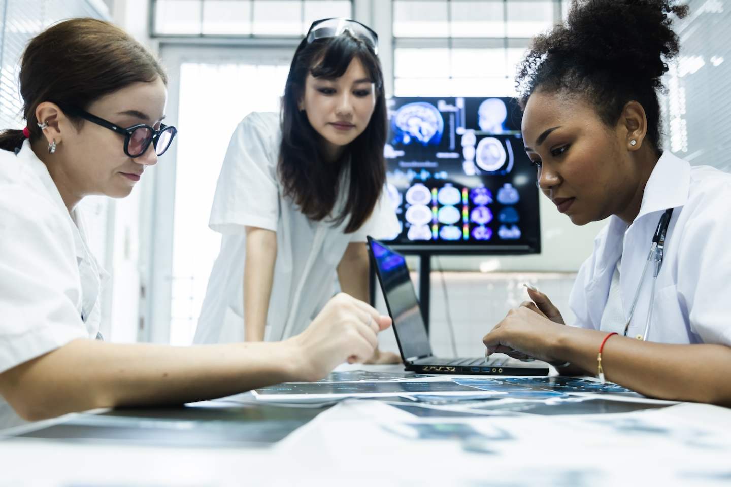 Team of female doctor check on scan results paper and looking at monitors in laboratory and plan and share medical knowledge and experience benefits her coworkers and patients