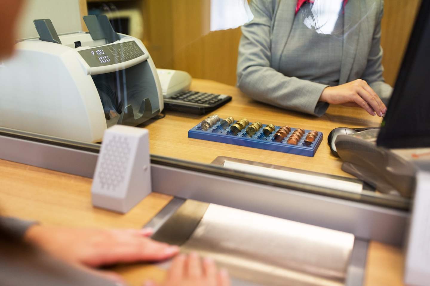 people, money, saving and finance concept - clerk counting coins for customer at bank office or currency exchanger