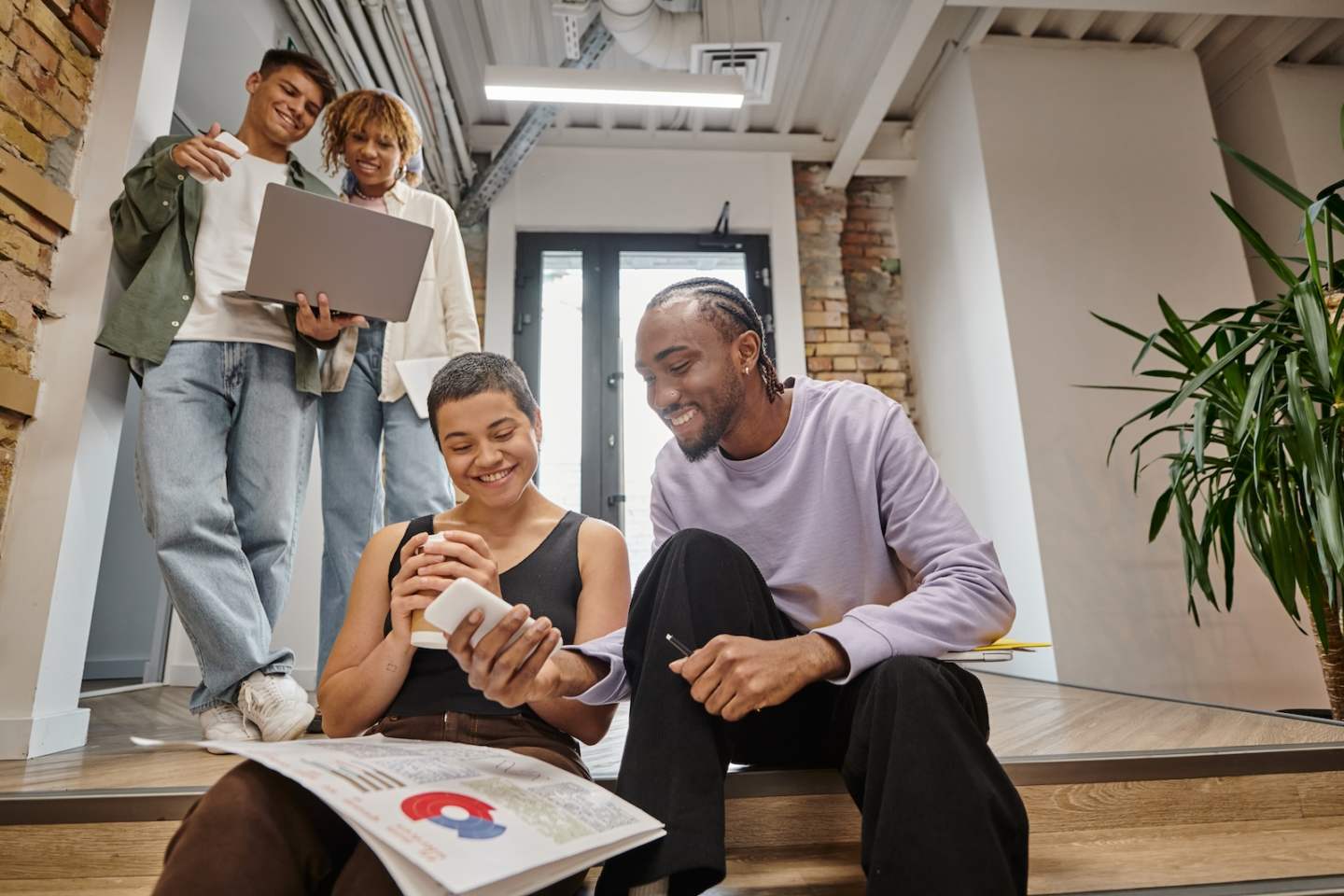 diverse colleagues looking at smartphone, graphs, project, startup, modern office, coworking, smile