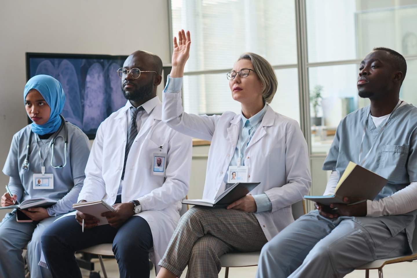 Group of doctors sitting on chairs with notepads asking questions and making notes during seminar