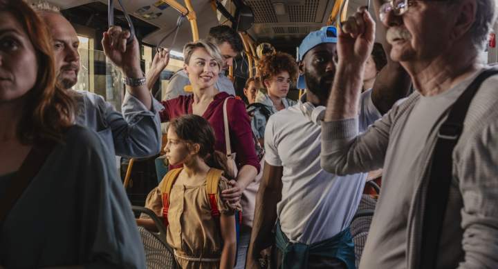 A crowded bus with diverse commuters standing and holding onto handrails during a busy ride.