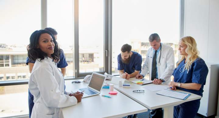 Black female doctor smiling at camera during a meeting with other doctors