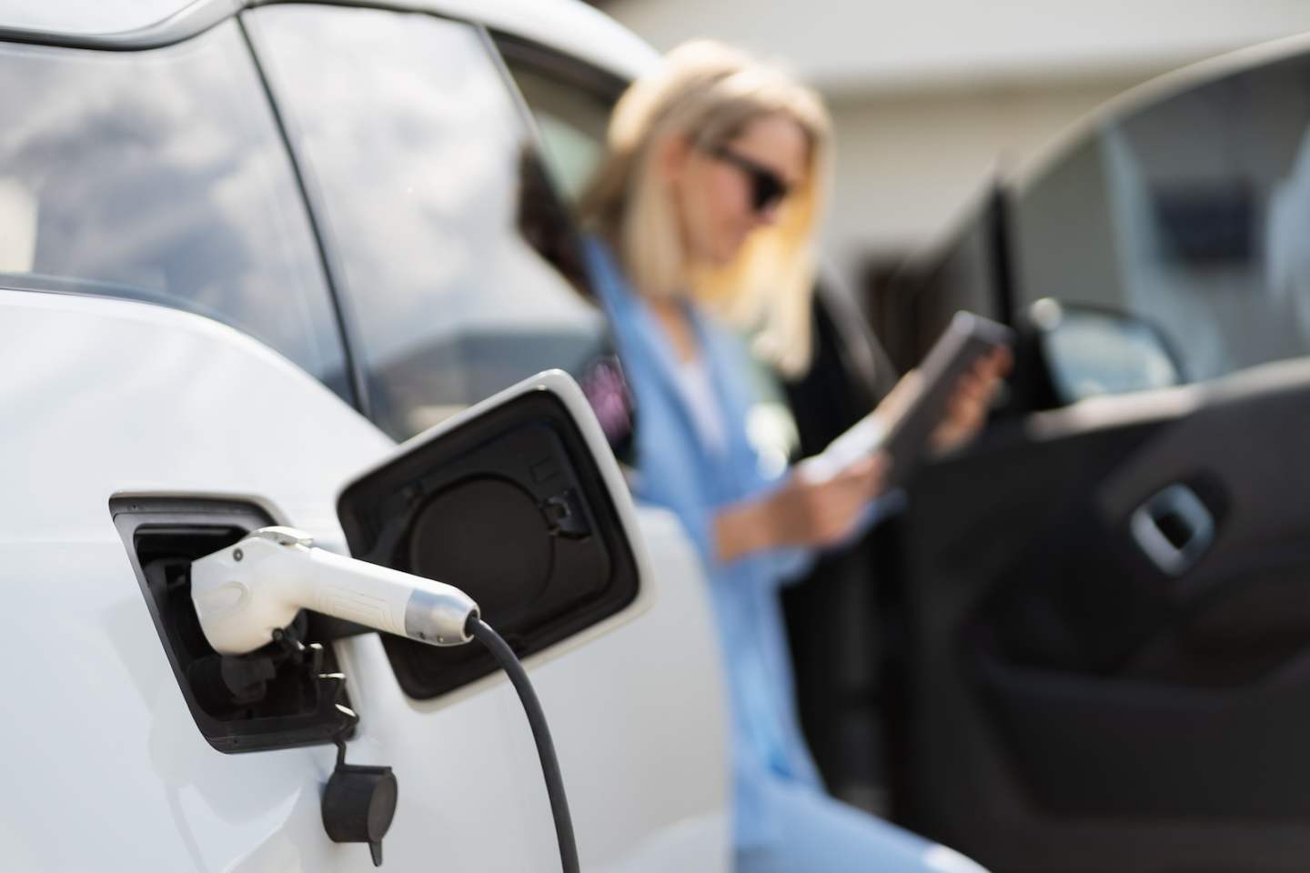 Woman Charging Electric Car While Using Tablet, Representing Modern Electric Vehicle Charging And Sustainable Energy