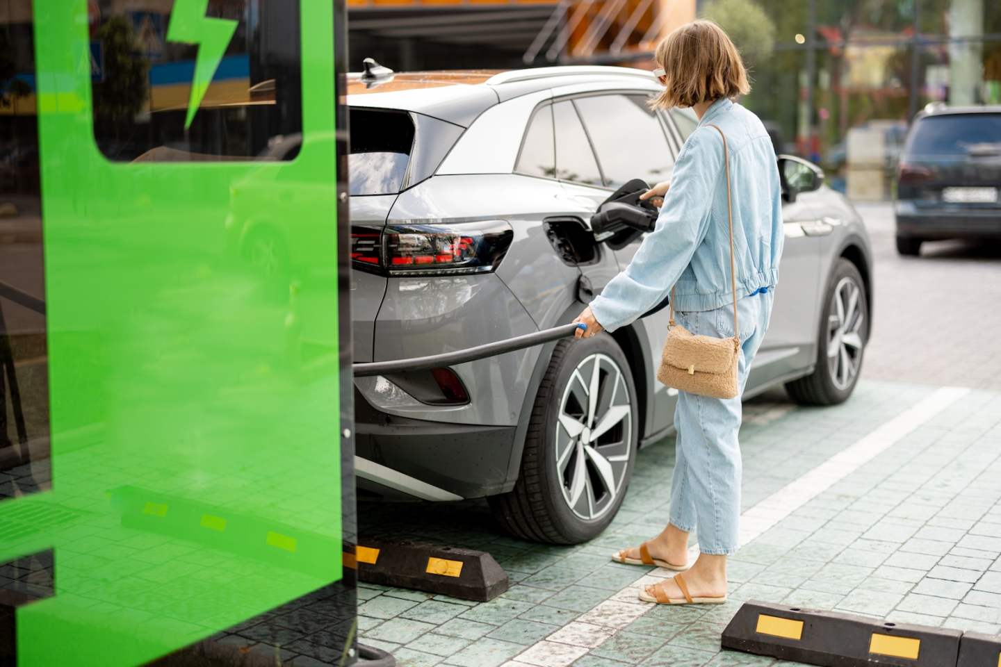 Young woman plugs in a cable for vehicle fast charging on a public charging station outdoors. Concept of electric car charging, electricity and green energy for driving