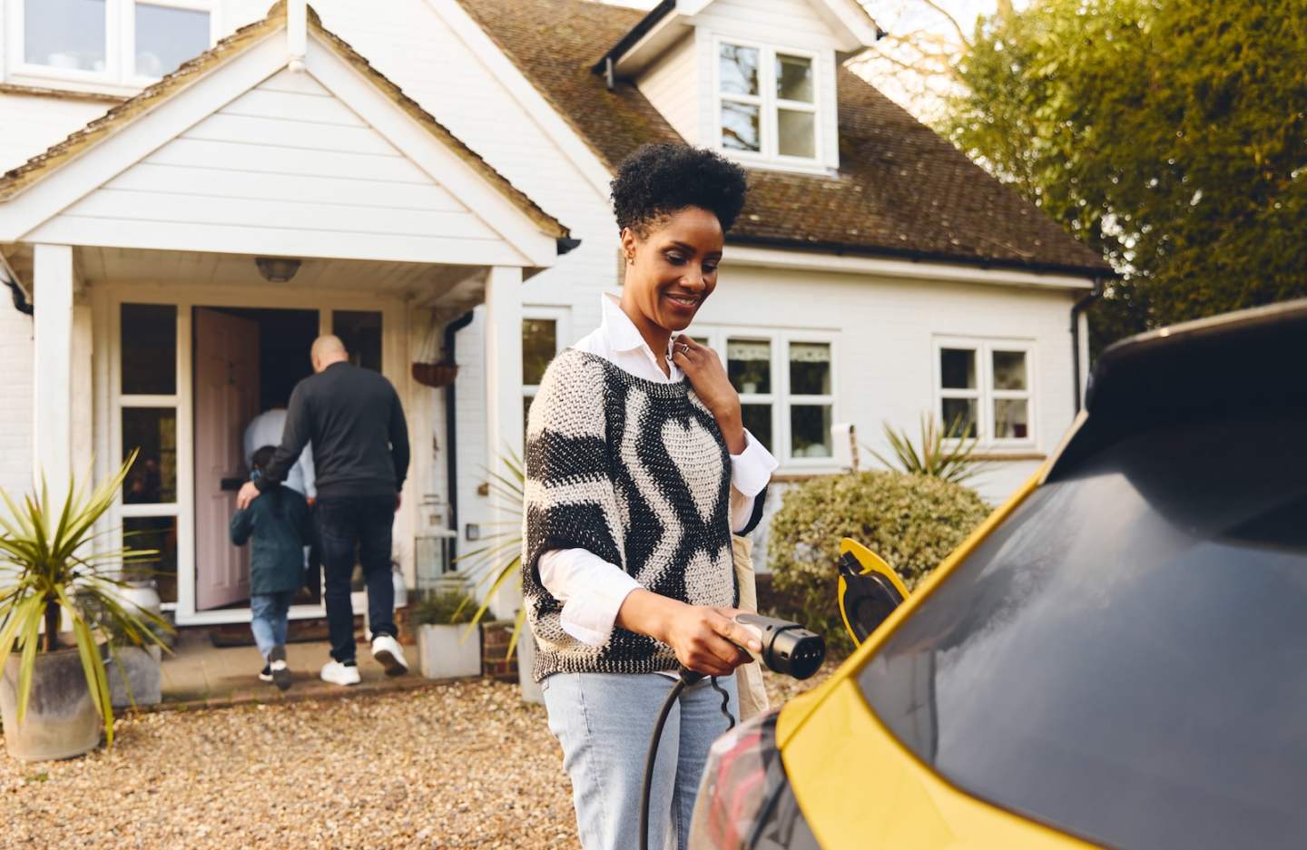 Woman plugging in electric charger into car With Family Outside House