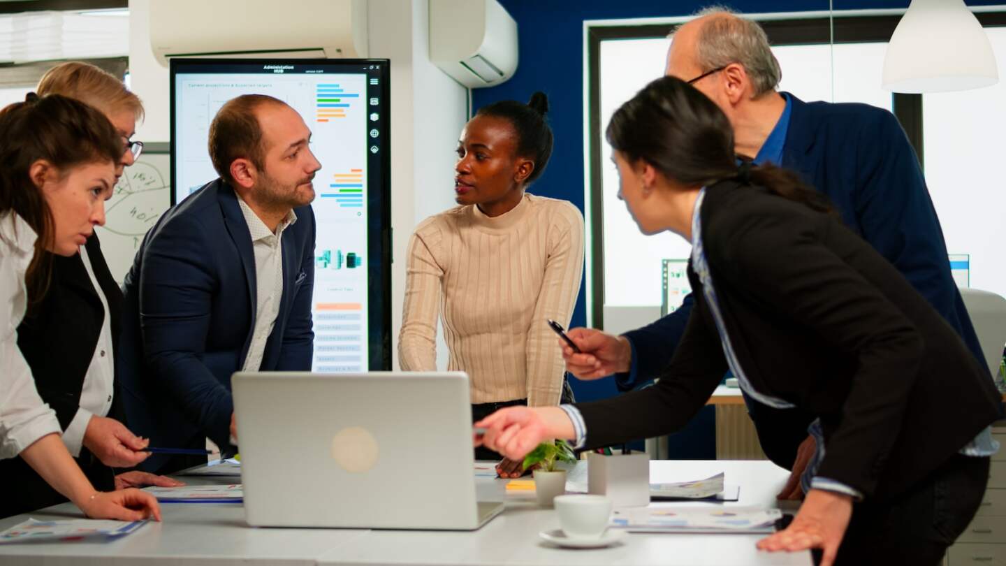 International business team talking to african woman mentor discussing company development plan standing at broadroom. Black leader explainig project strategy to diverse multiracial corporate group