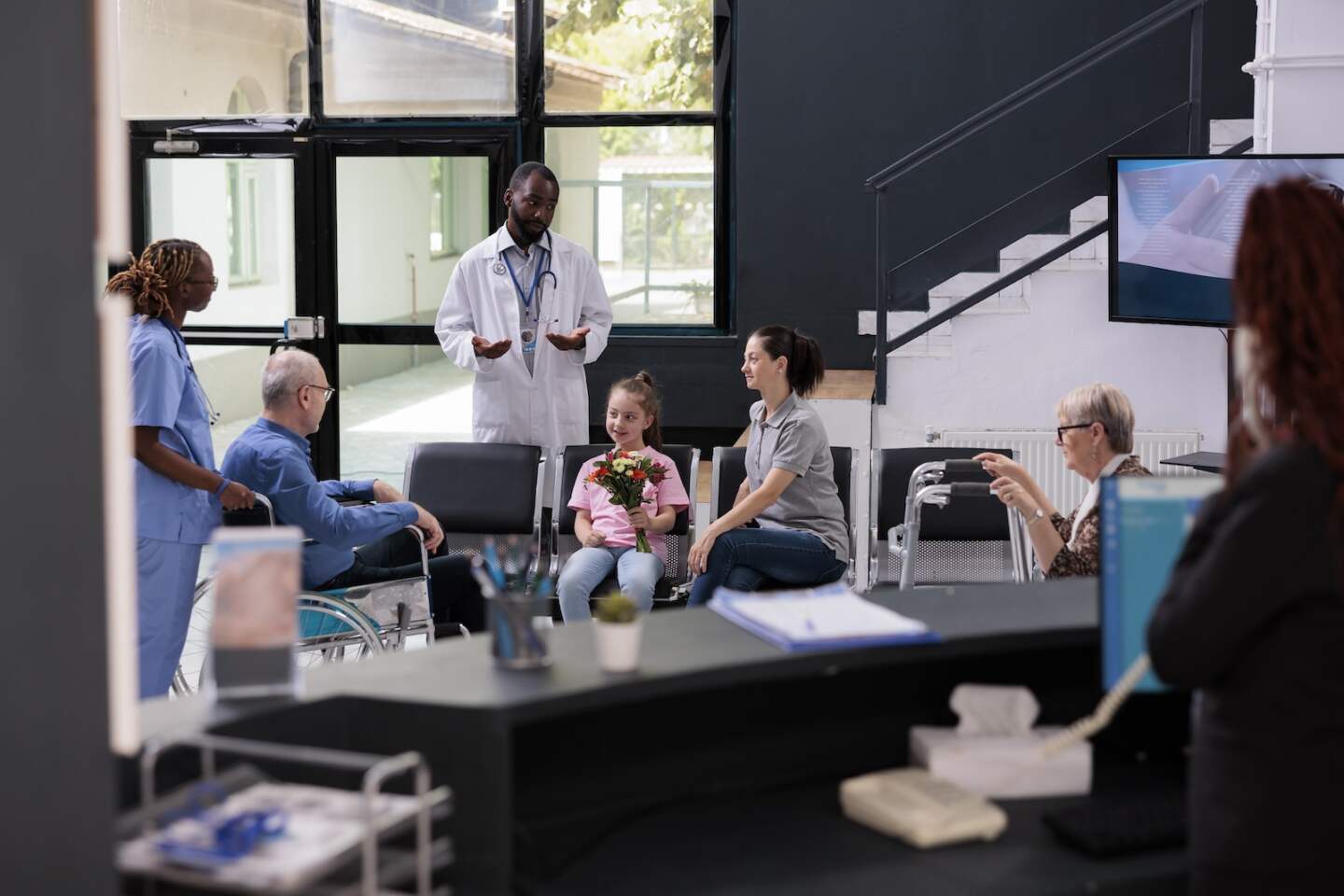 Nurse bringing senior man after finishing consultation while doctor explaining health care treatment to family in hospital waiting area. Little girl holding flowers for grandfather. Medicine service