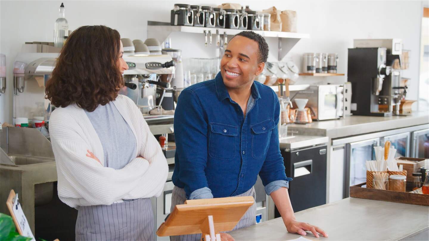 Smiling Male And Female Owners Or Workers Behind Counter In Coffee Shop