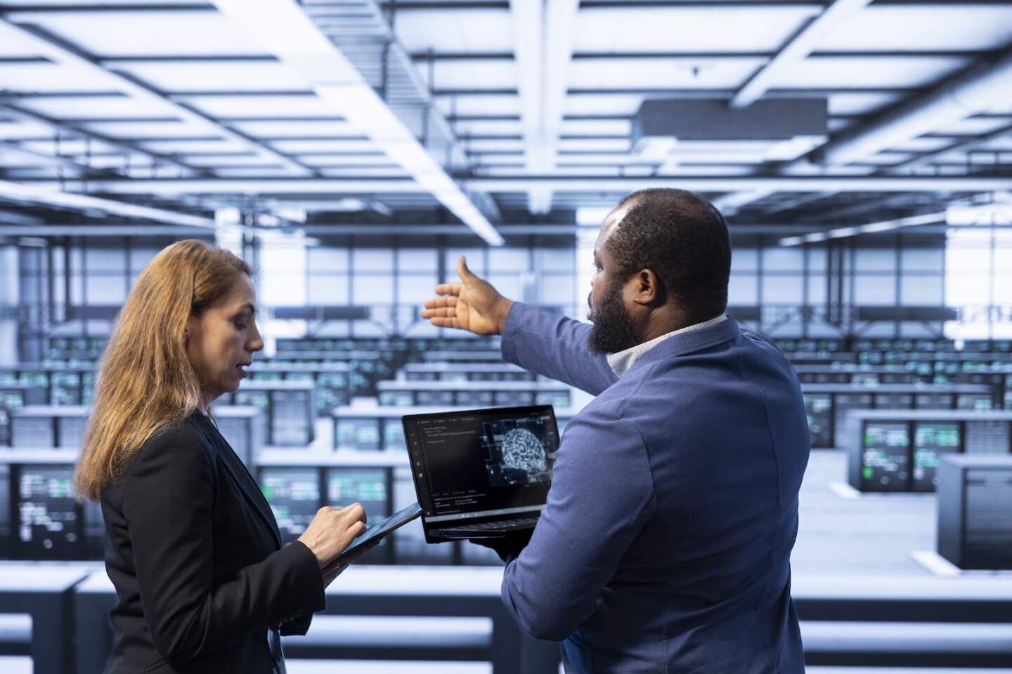 Team of technicians in data center using laptop to visualize artificial intelligence neural networks made up of interconnected nodes. Teamworking colleagues oversee AI systems processing information