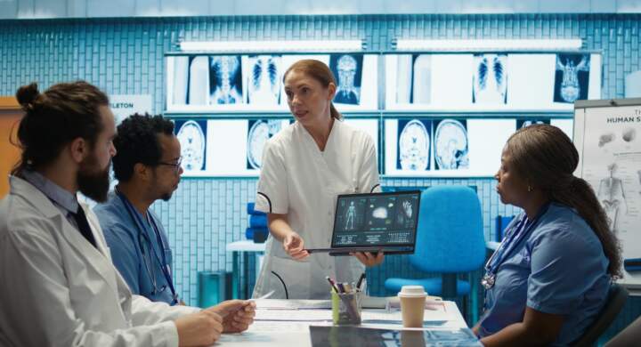 Diverse medical team examining test results and discussing innovative treatment plans at a modern clinic to enhance patient care quality. Doctors and nurses review x ray scans. Camera B.